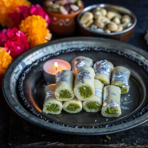kaju pista rolls arranged on a plate with candles, diyas and flowers in the background