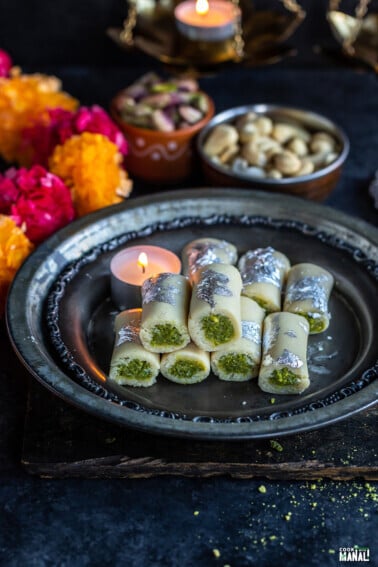 kaju pista rolls arranged on a plate with candles, diyas and flowers in the background