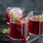 red color drink in a glass topped with fresh cranberries and rosemary