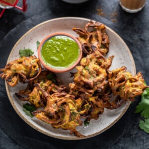 onion pakoda in a plate with a bowl of cilantro chutney