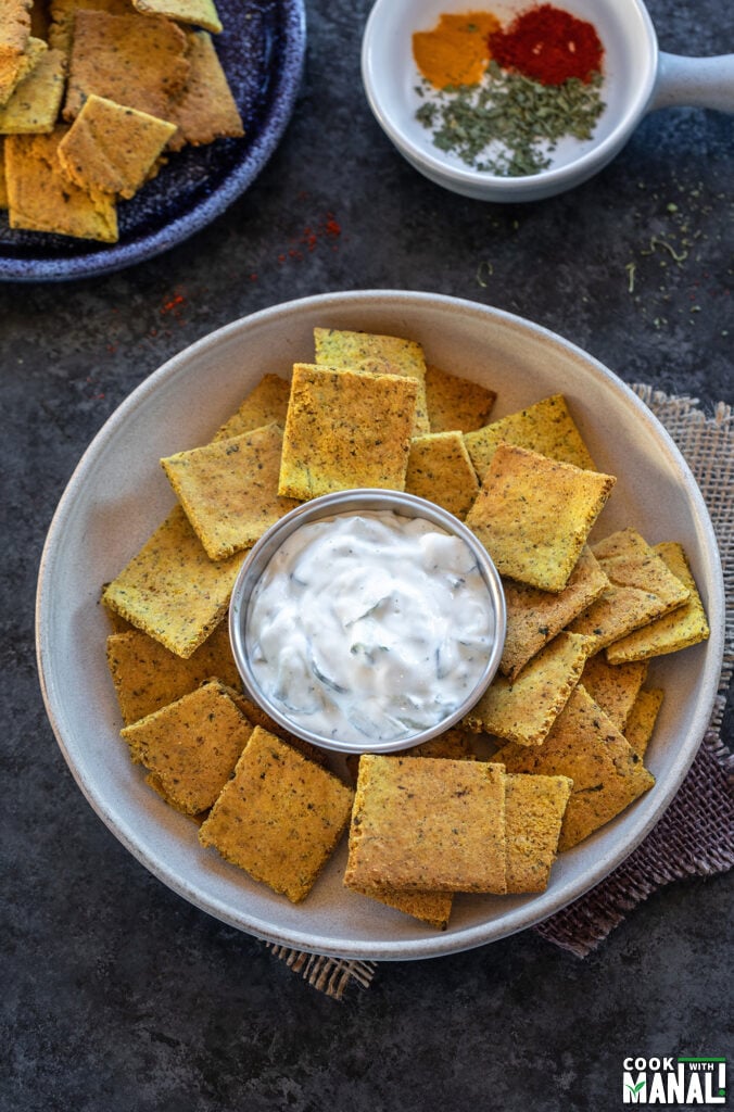 bowl with yellow color masala crackers served with white sauce