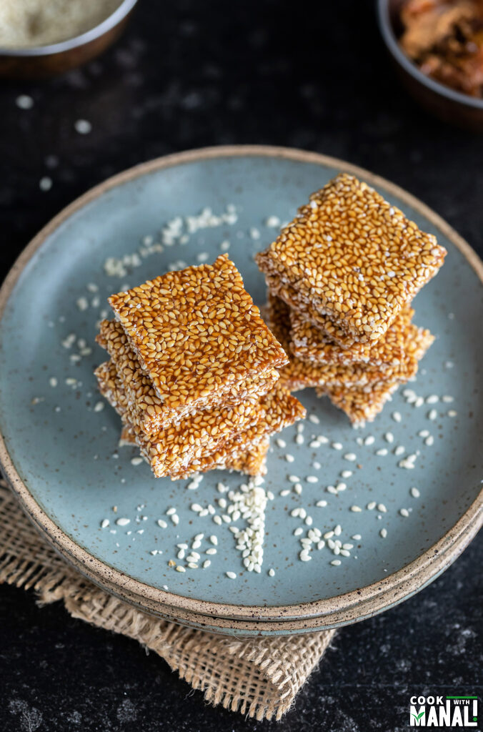 stacks of til chikki arranged on a blue plate with white sesame seeds scattered all around