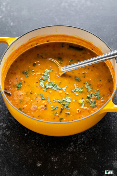 dal in a yellow color pot with ladle and garnished with cilantro