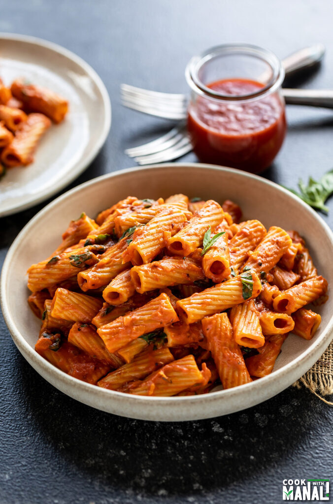 rigatoni pasta served in a white round bowl, with jar of tomatoes in the background
