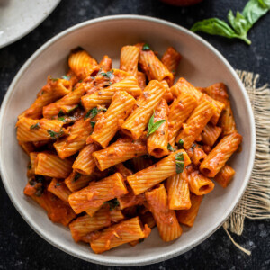 rigatoni pasta served in a white round bowl, garnished with basil