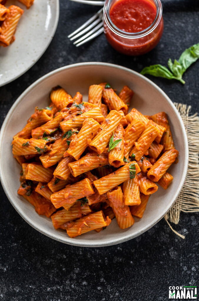 rigatoni pasta served in a white round bowl, garnished with basil