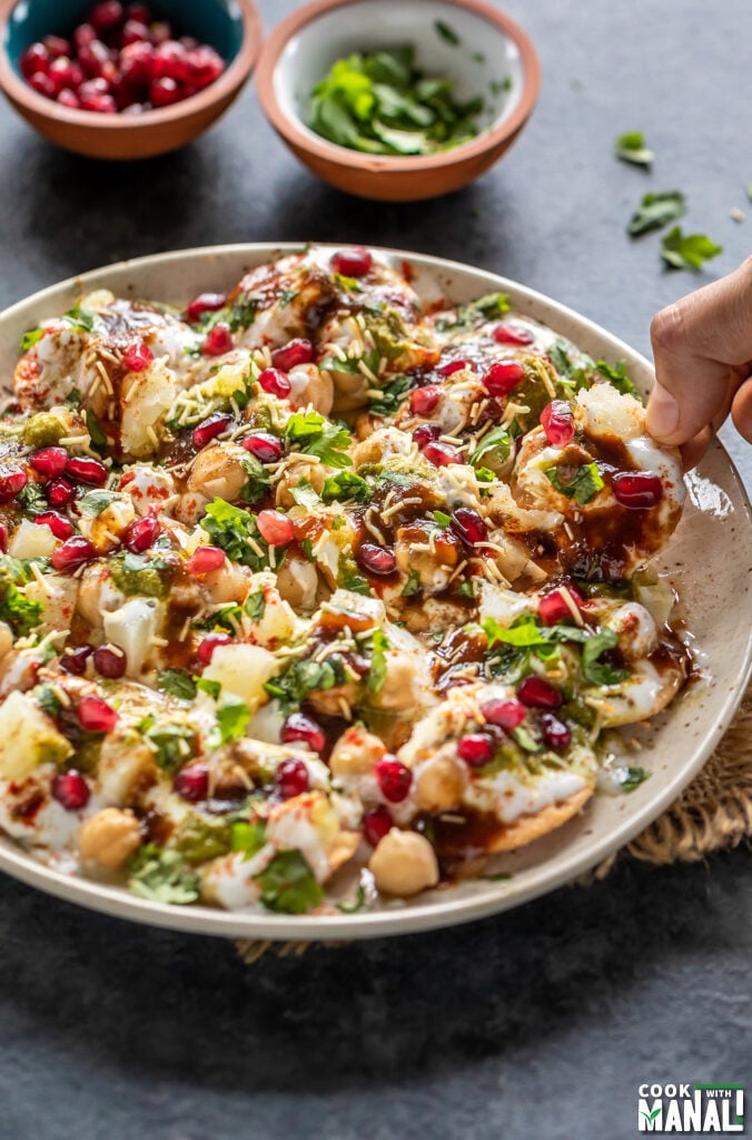 hand picking up one of the papdis from a plate of papdi chaat