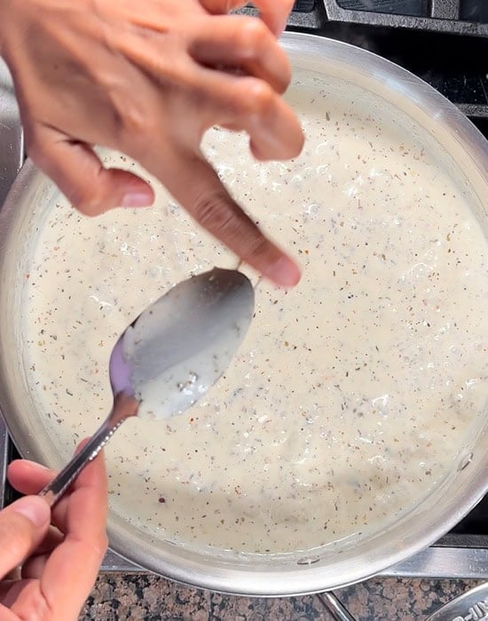 a finger brushing the back of a spoon to show the thickness of the sauce