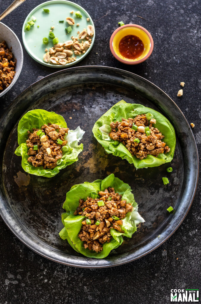 3 tofu lettuce wraps arranged on a black plate with small bowls placed in the background