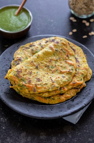 stack of oats chilla served on a black plate with a bowl of chutney in the background