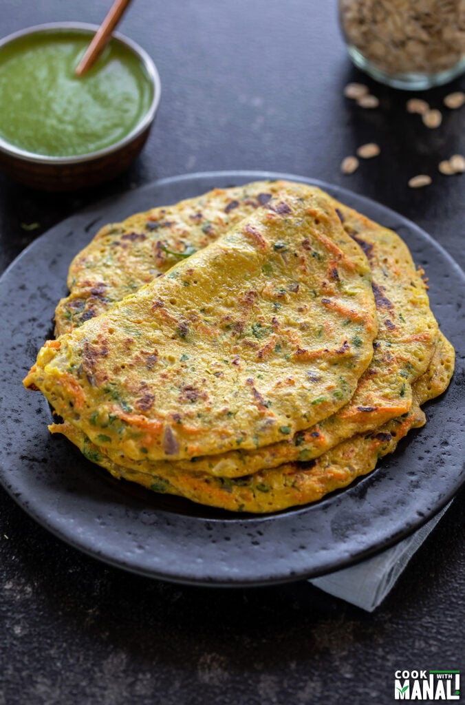 stack of oats chilla served on a black plate with a bowl of chutney in the background