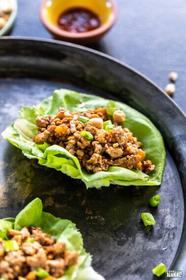 tofu lettuce wrap topped with green onions with bowls of sauce in the background