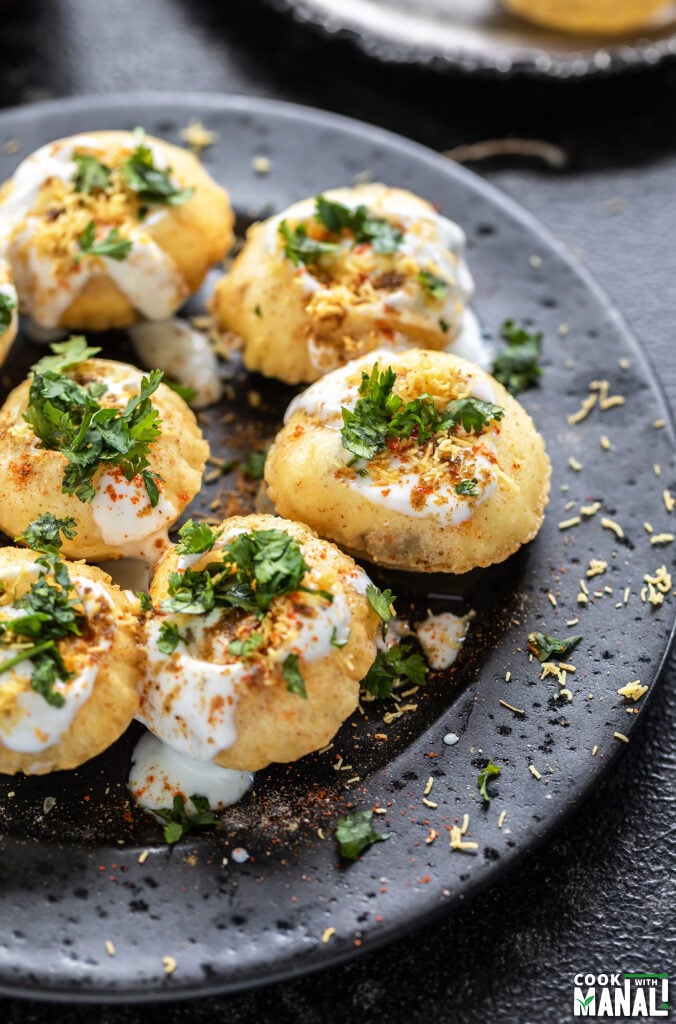 dahi puri topped with cilantro and sev arranged on a black plate