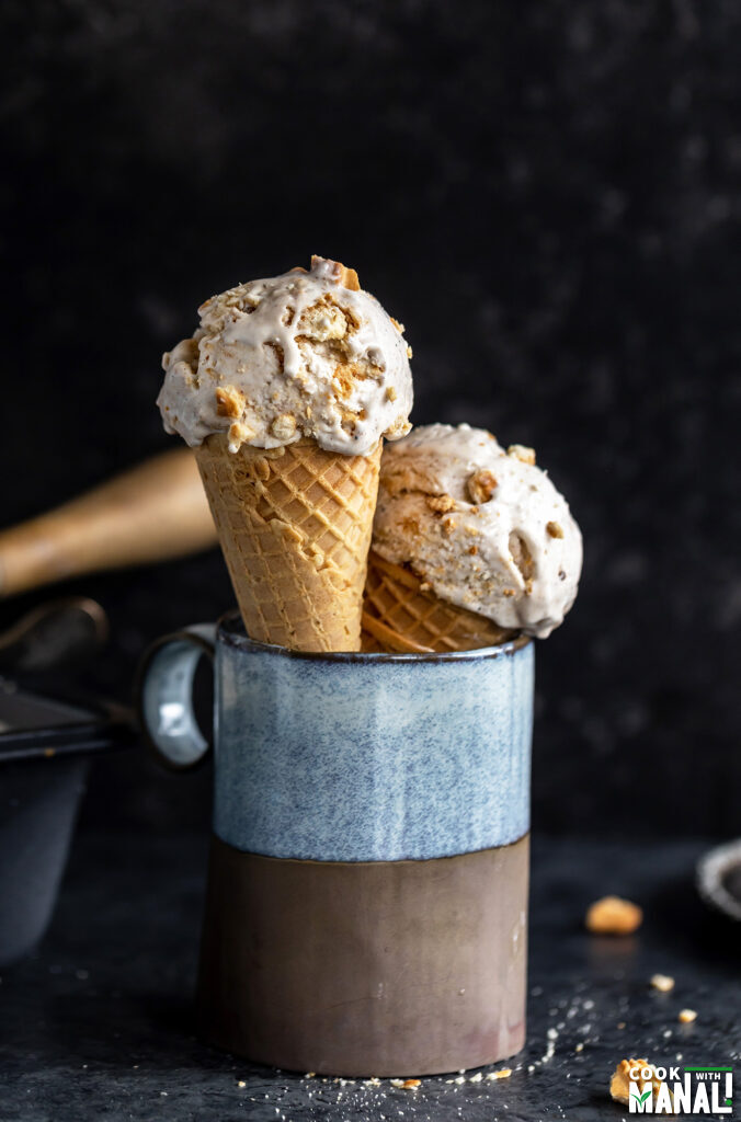 2 cones of ice cream in a blue mug with some crushed cookies scattered around