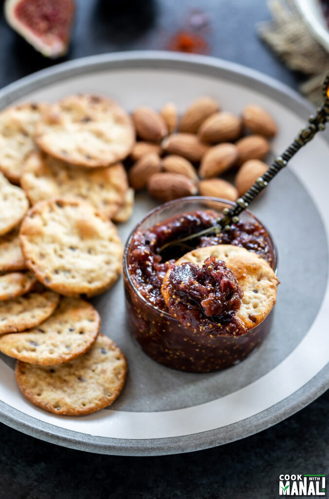 cracker dipped in a bowl of fig chutney with more crackers and almonds on the plate