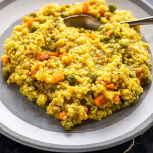 vegetable daliya served on a white plate with spoon on the side