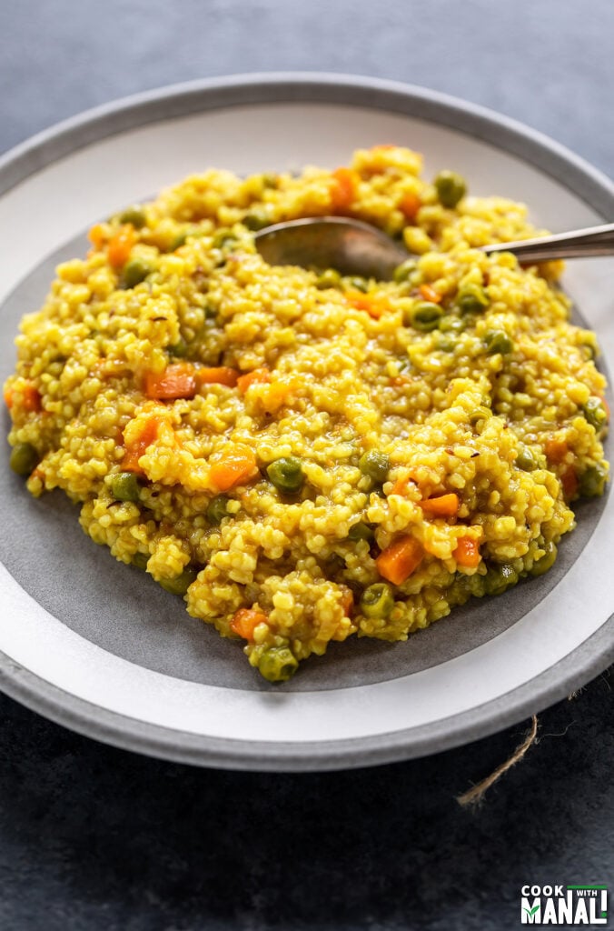 vegetable daliya served on a white plate with spoon on the side