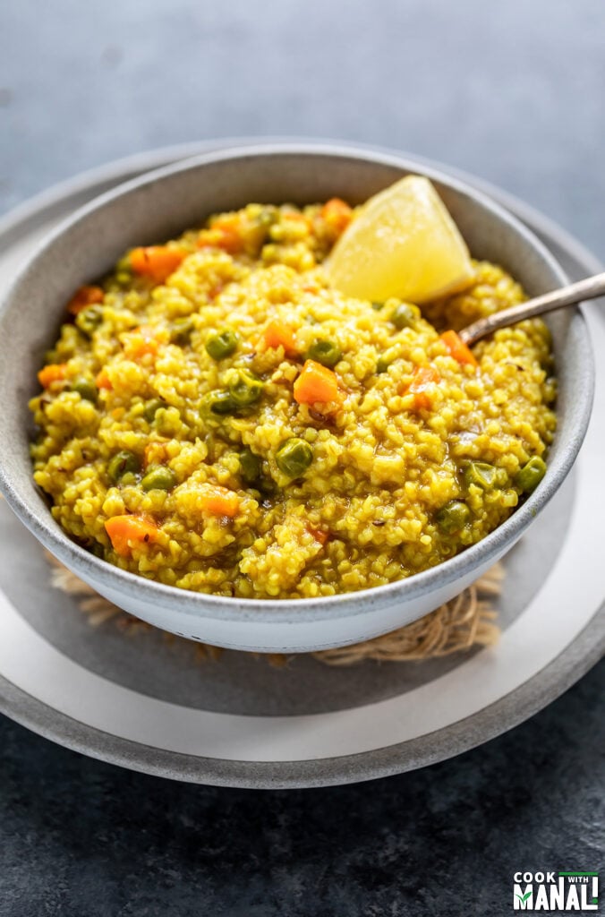 vegetable daliya in a bowl with a side of lemon wedge