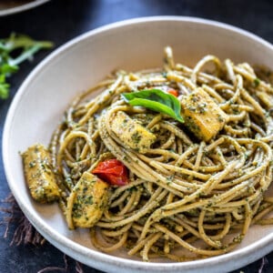 bowl of spaghetti tossed with pesto and paneer, garnished with basil