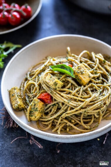 bowl of spaghetti tossed with pesto and paneer, garnished with basil