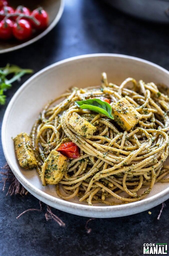 bowl of spaghetti tossed with pesto and paneer, garnished with basil