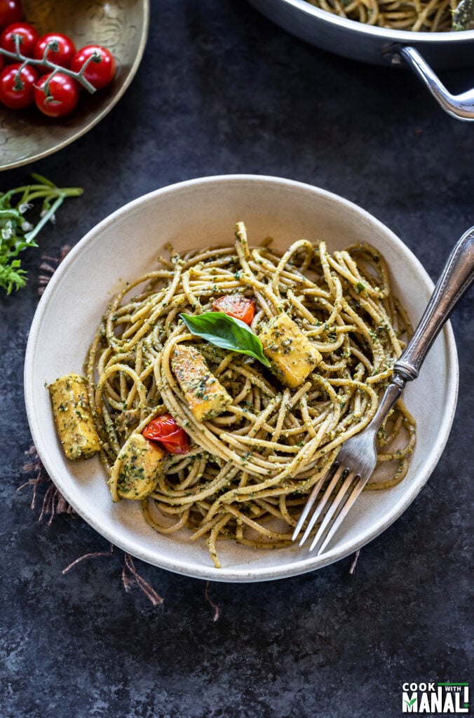 bowl of spaghetti tossed with pesto with a fork placed on the side of the bowl