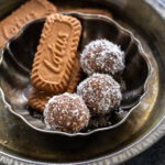 three biscoff ladoo arranged in a plate with biscoff cookies placed on one side