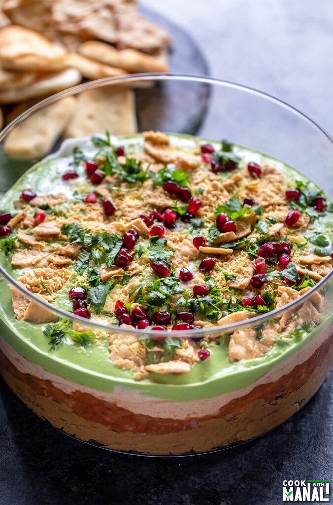 layered dip served in a transparent bowl topped with cilantro, pomegranate