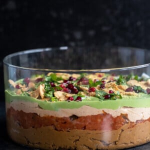 layered dip served in a transparent bowl topped with cilantro, pomegranate