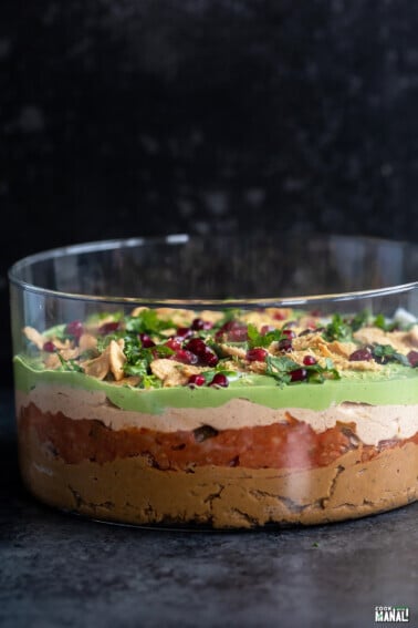 layered dip served in a transparent bowl topped with cilantro, pomegranate