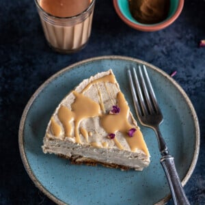 slice of masala chai cheesecake garnished with rose petals and served on a blue plate