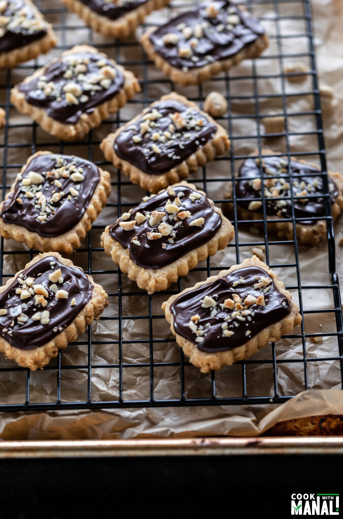 cookies topped with chocolate and hazelnuts arranged on a cooling rack 