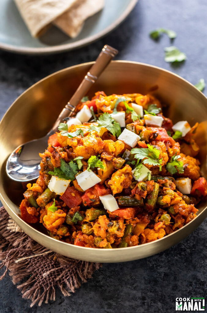 mixed vegetables cooked with spices and served in a brass bowl with spoon placed on the side