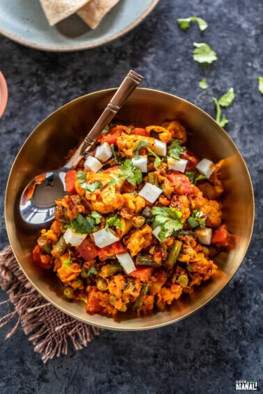 mixed vegetables cooked with spices and served in a brass bowl with spoon placed on the side