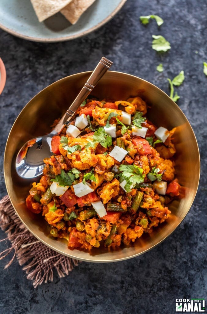 mixed vegetables cooked with spices and served in a brass bowl with spoon placed on the side