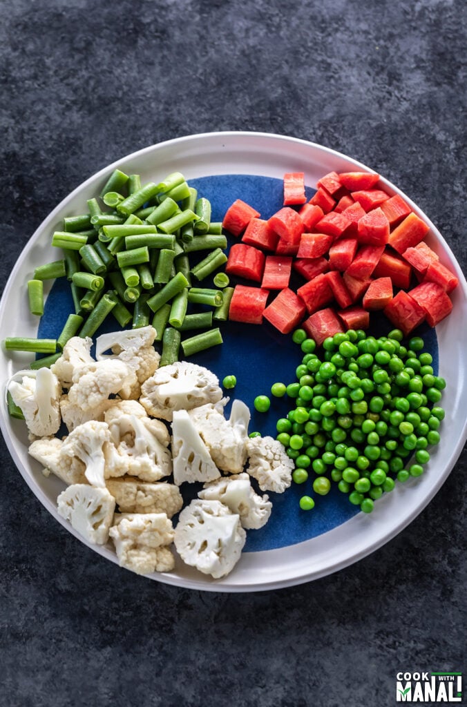 cut cauliflower, carrots, peas and beans arranged on a plate