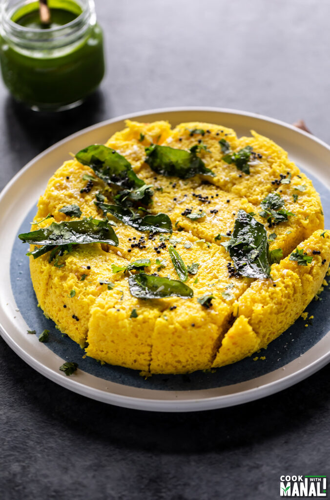 cut dhokla pieces in a plate topped with tadka of curry leaves and mustard seeds
