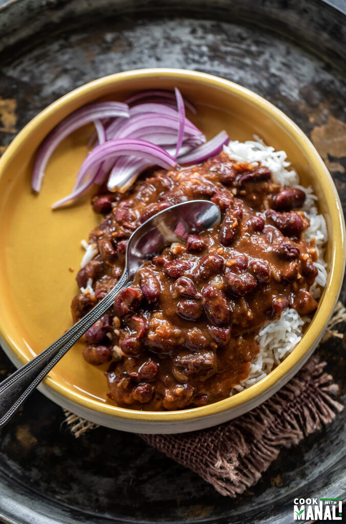 rajma served over rice in a yellow color bowl with sliced onions on the side