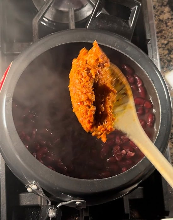 masala being added to a cooker with rajma in it