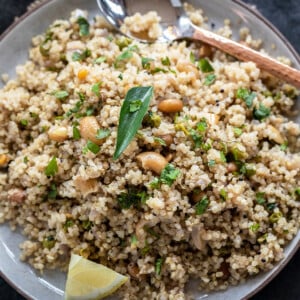 Quinoa upma served in a plate topped with curry leaves, lemon wedge and a copper spoon placed on the side