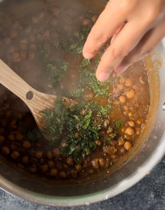 a hand adding fresh cilantro to pot of chole