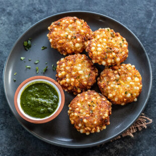 5 pieces of sabudana vada arranged in a plate with a small bowl of cilantro chutney on the side