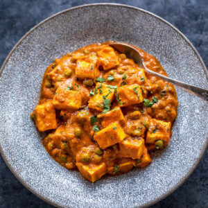 matar paneer served in a bowl with spoon on the side