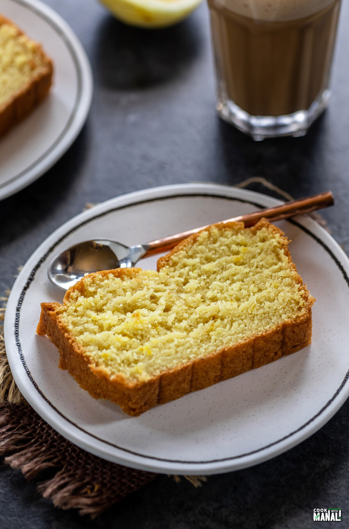 slice of lemon cake placed on a white plate with copper spoon on the side