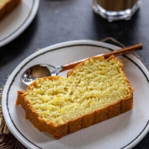 slice of lemon cake placed on a white plate with copper spoon on the side