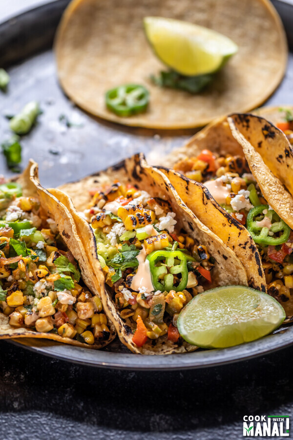 grilled corn tacos arranged on a plate with a lime wedge placed on the side