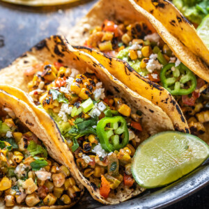 grilled corn tacos arranged on a plate with a lime wedge placed on the side