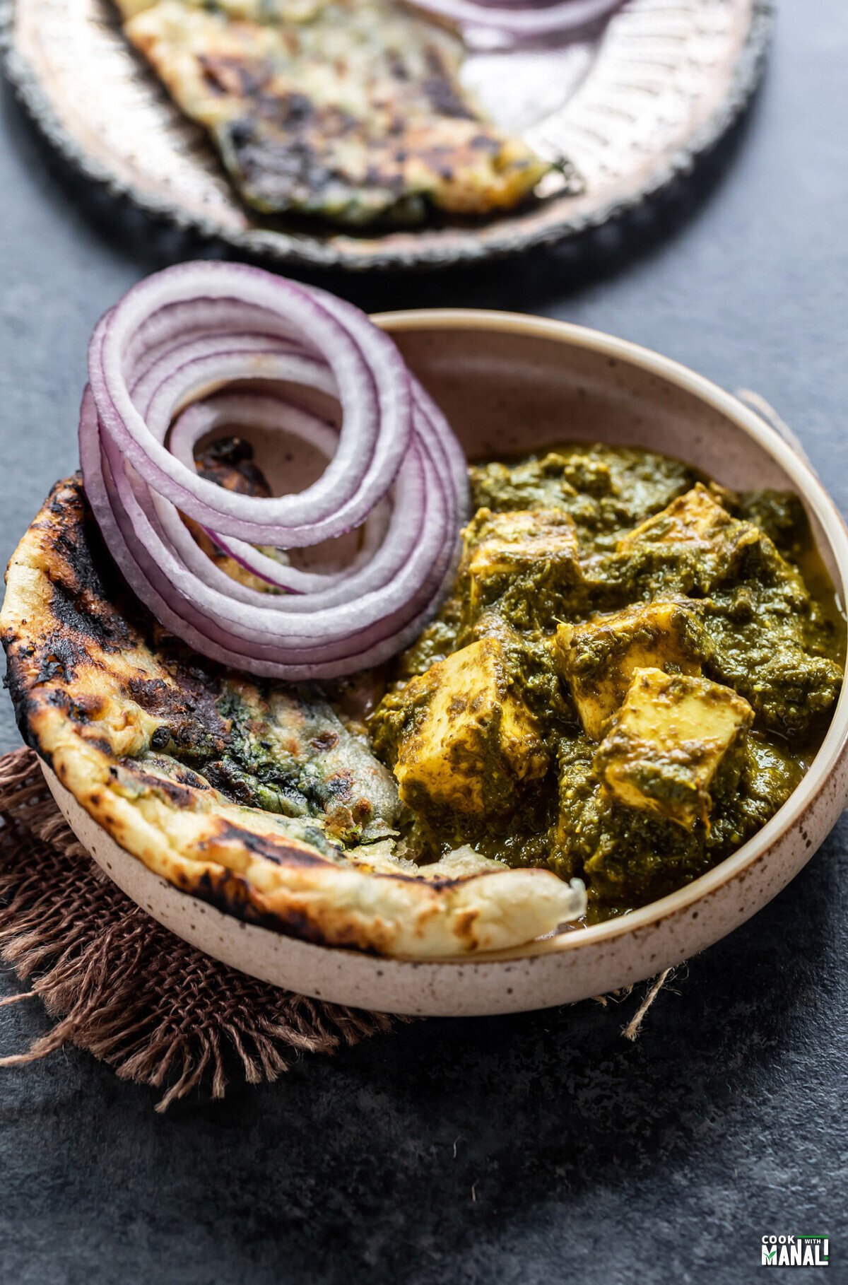 saag paneer served with a side of naan and onion slices in a round bowl