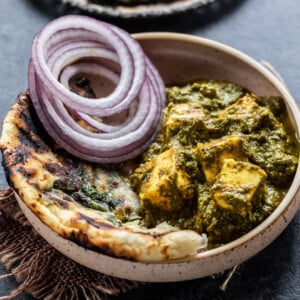 saag paneer served with a side of naan and onion slices in a round bowl