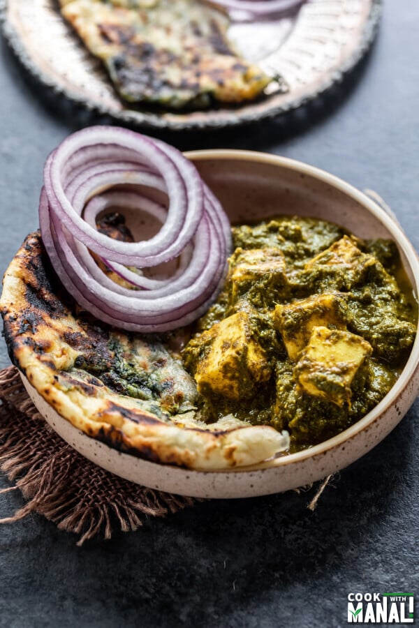 saag paneer served with a side of naan and onion slices in a round bowl